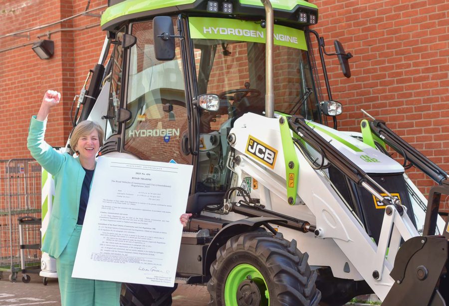 Firma del decreto per l’idrogeno: Lilian Greenwood, Ministro per il Futuro delle Strade, posa accanto alla terna JCB a idrogeno esibendo il documento ufficiale che modifica la normativa per consentire la circolazione delle macchine operatrici a idrogeno